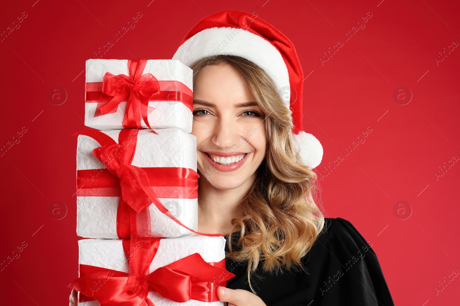 Photo of Beautiful young woman in Santa hat with Christmas presents on red background