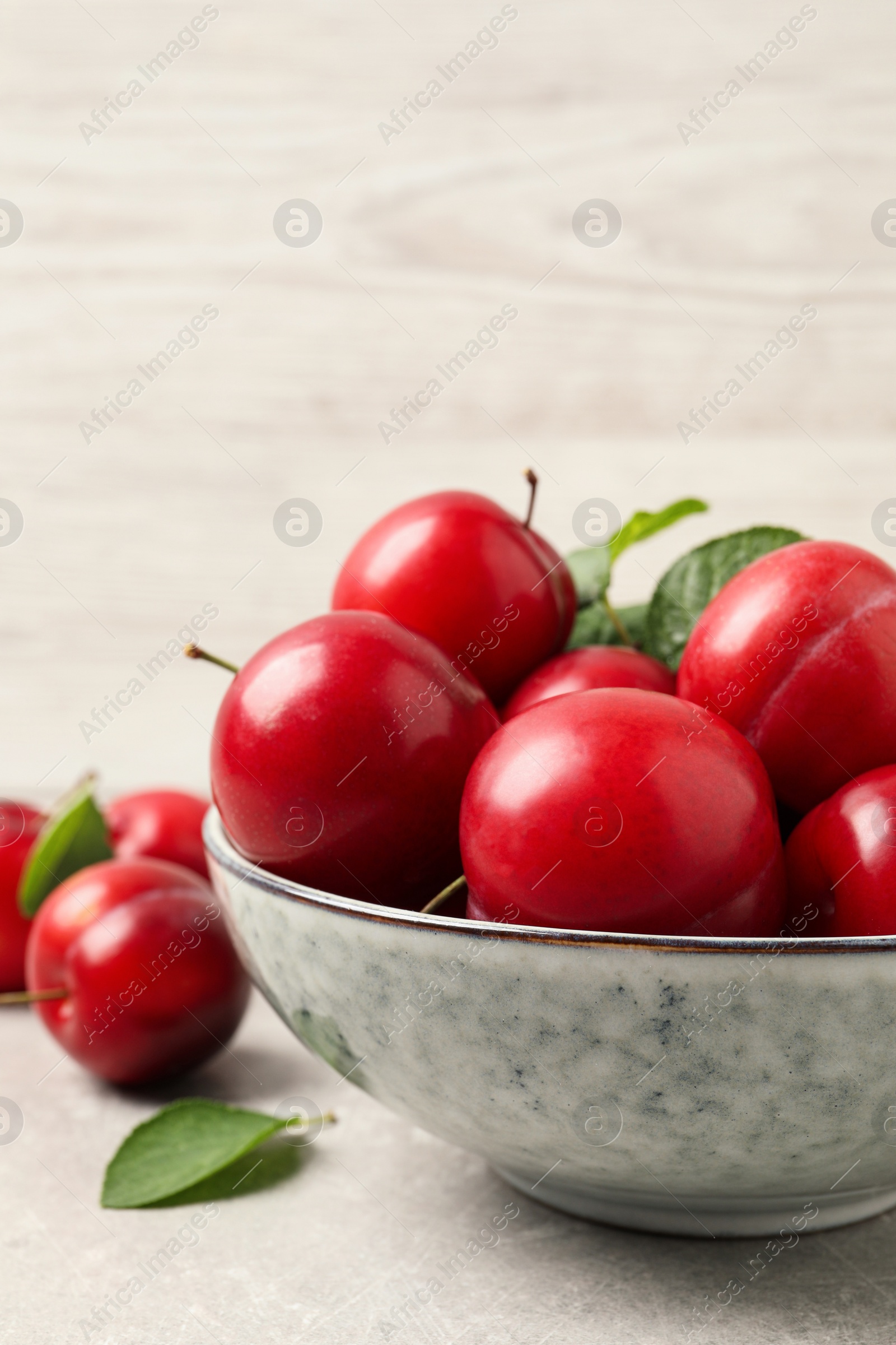 Photo of Delicious ripe cherry plums with leaves on light table, closeup