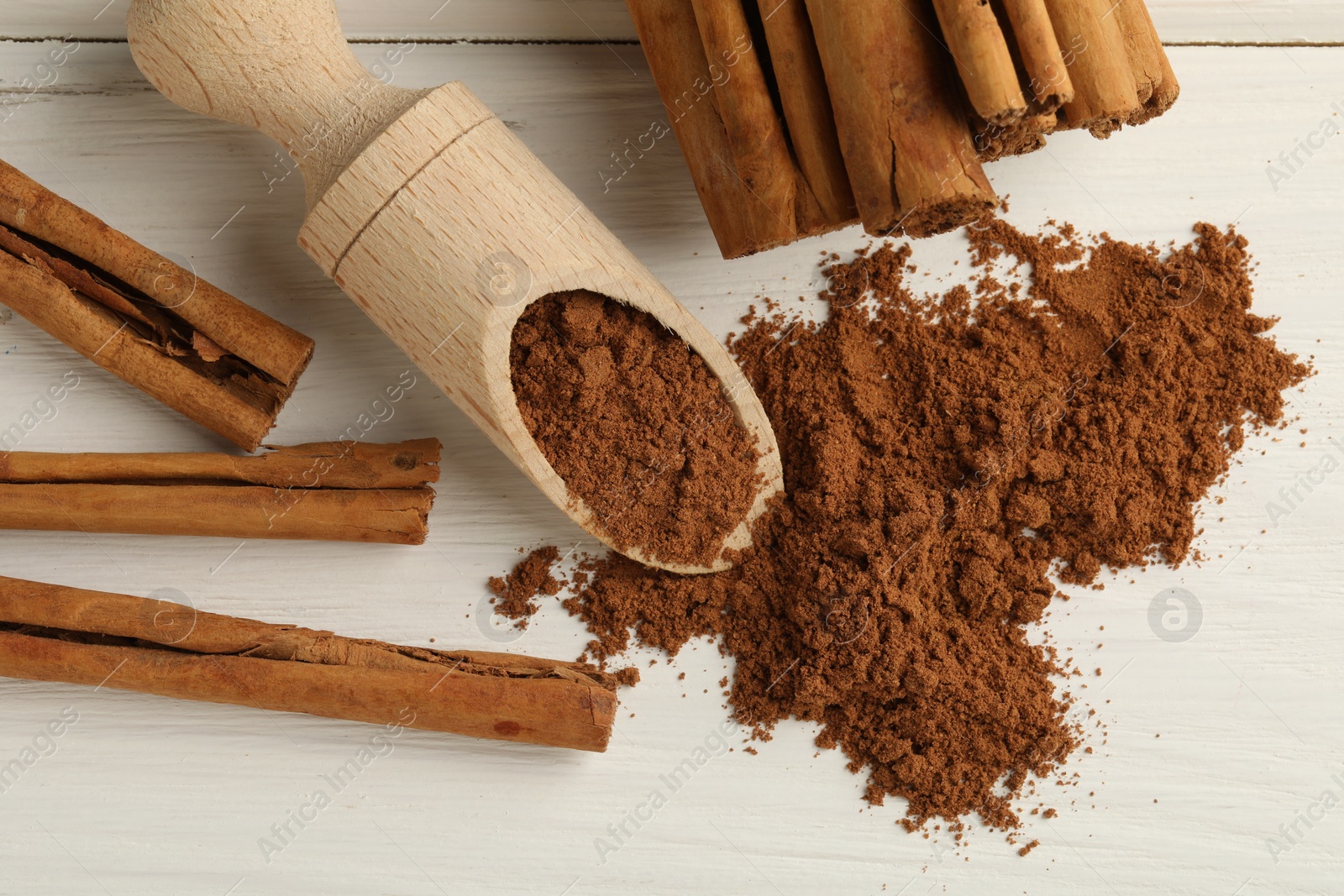 Photo of Dry aromatic cinnamon sticks, powder and scoop on white wooden table, flat lay