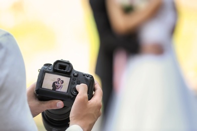 Photo of Professional photographer with camera and wedding couple, outdoors