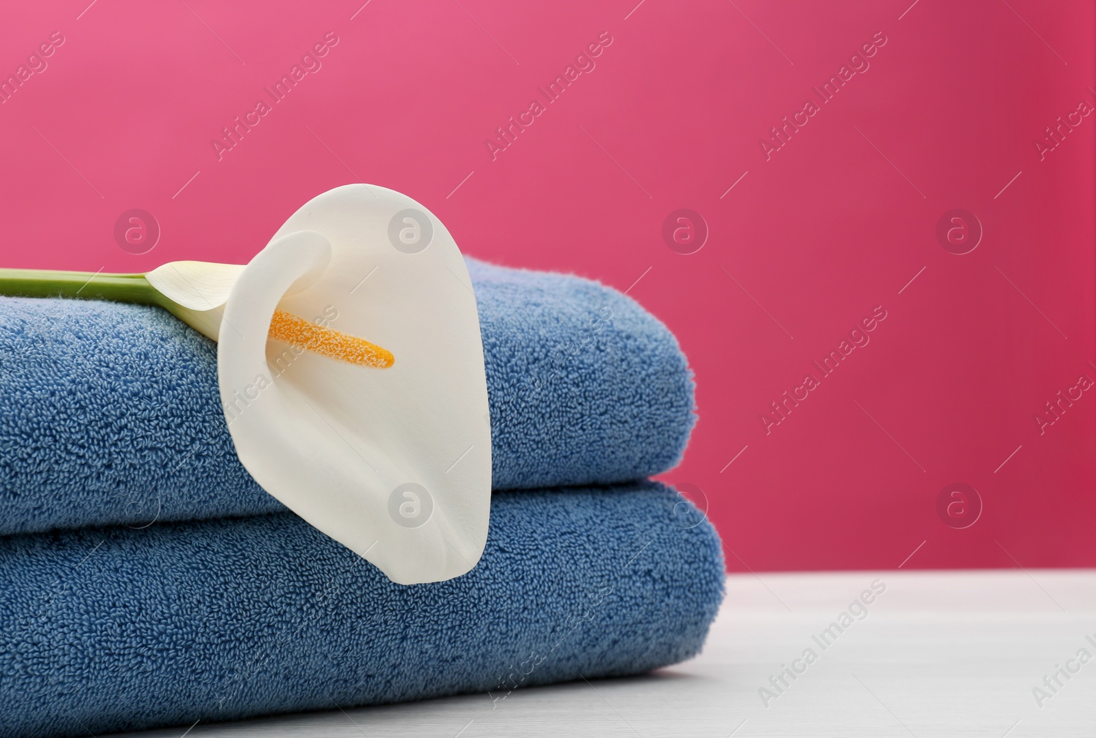 Photo of Soft clean towels with beautiful flower on table against color background. Space for text