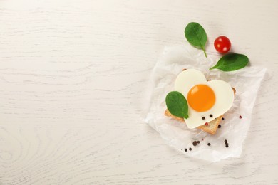 Photo of Heart shaped fried egg with toast, spinach and tomatoes on white wooden table, flat lay. Space for text