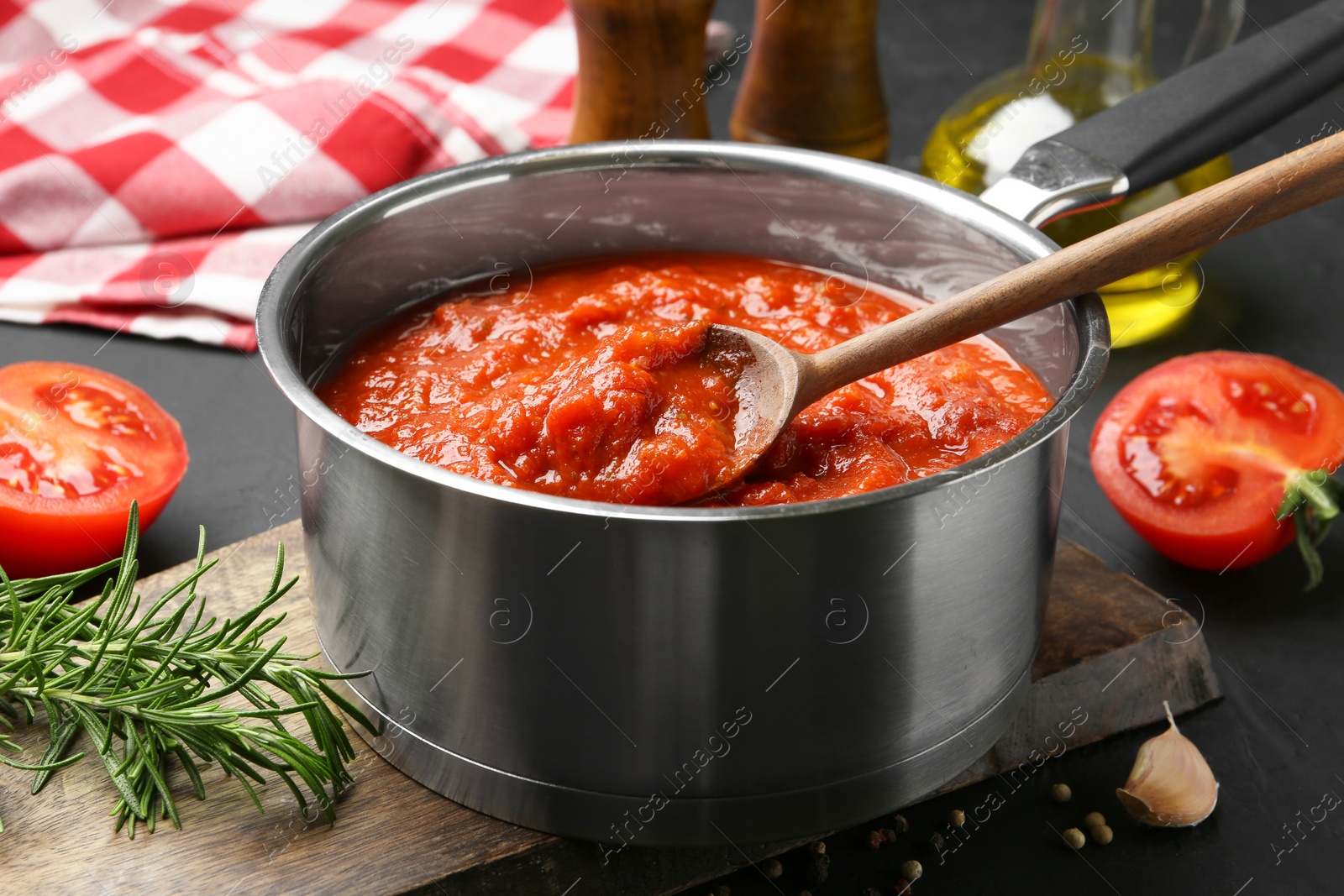 Photo of Homemade tomato sauce in pot, spoon and ingredients on dark table