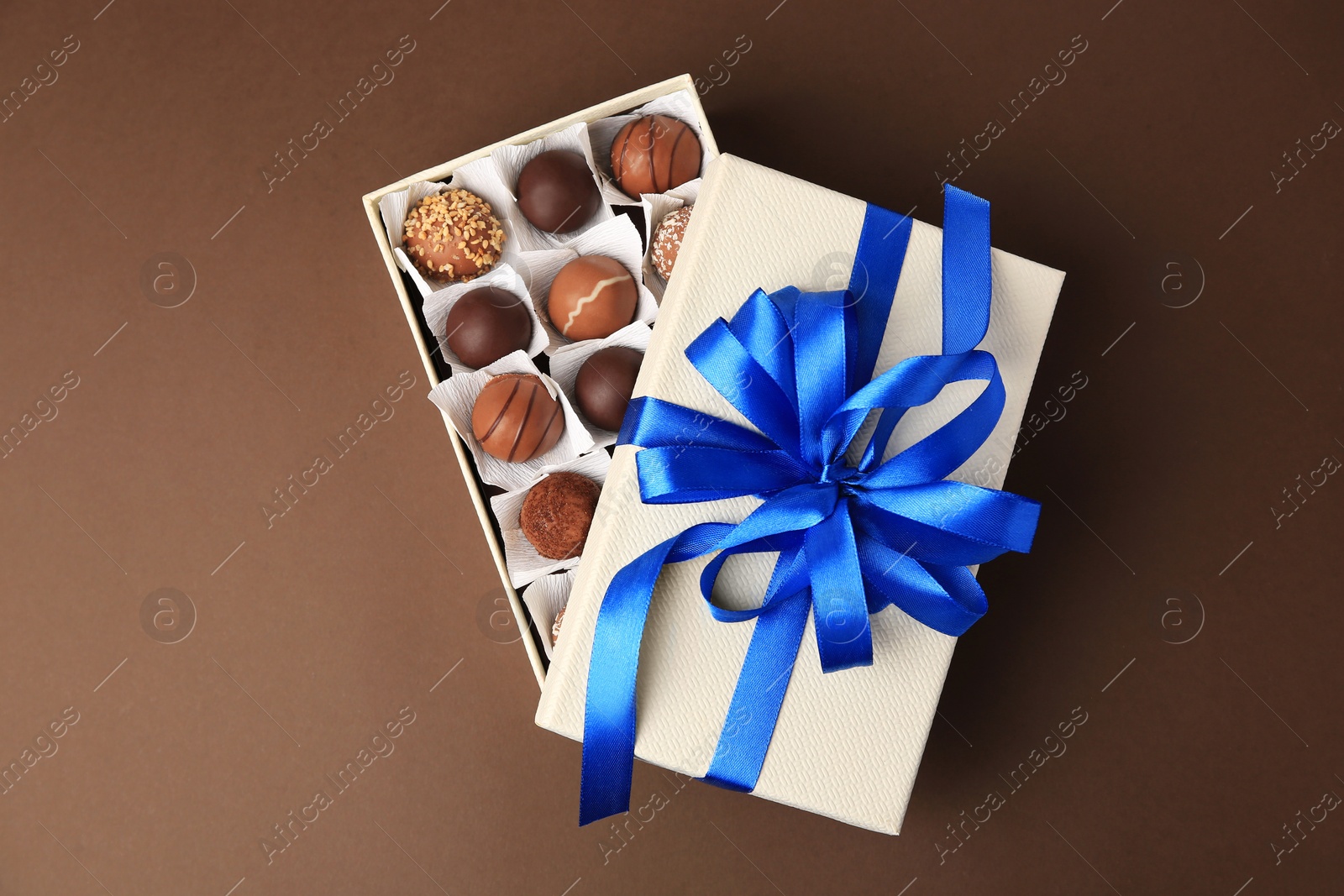 Photo of Box with delicious chocolate candies on brown background, top view