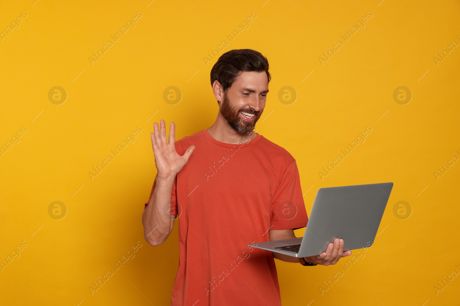 Photo of Handsome man with laptop on orange background