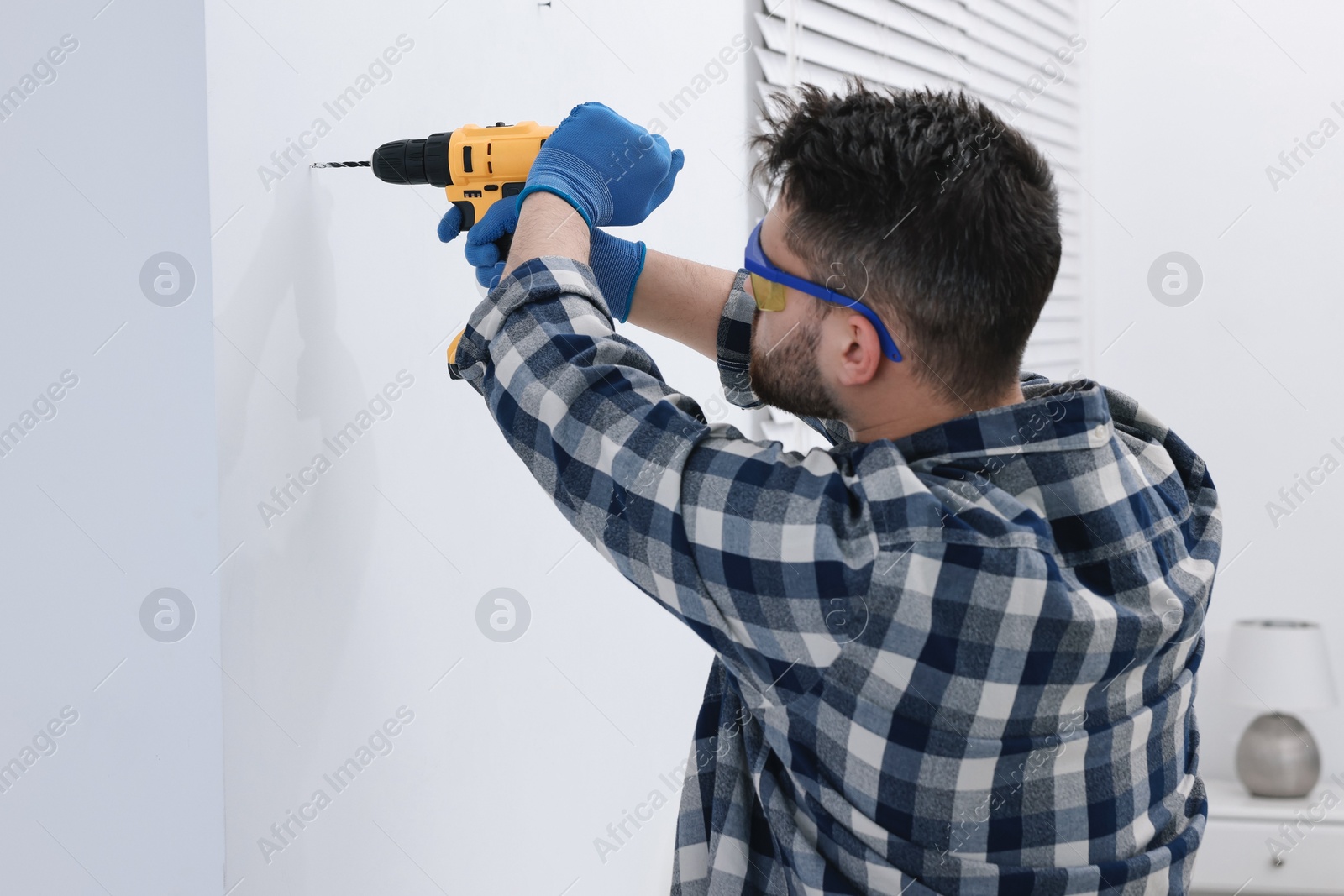 Photo of Young handyman working with electric drill at home