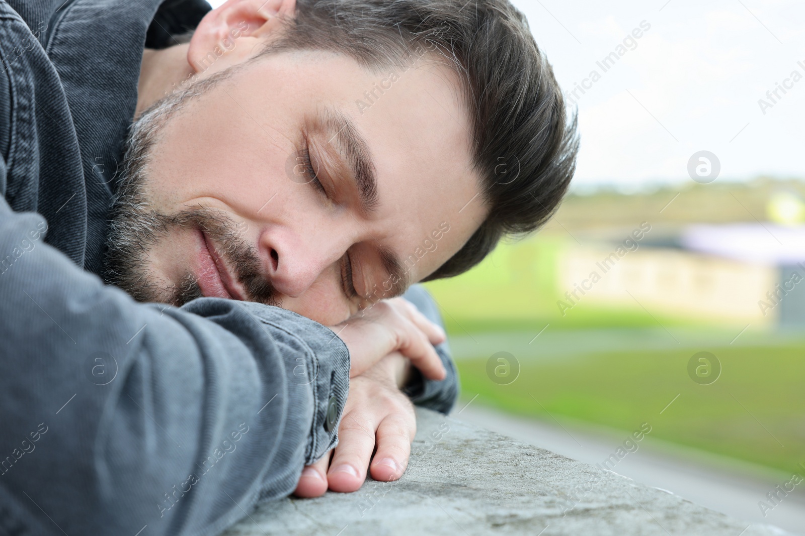 Photo of Tired man sleeping on stone parapet outdoors, closeup. Space for text