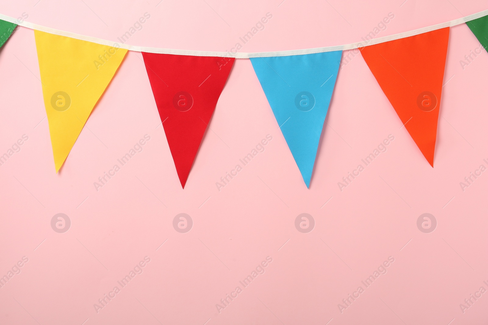 Photo of Bunting with colorful triangular flags on pink background. Space for text