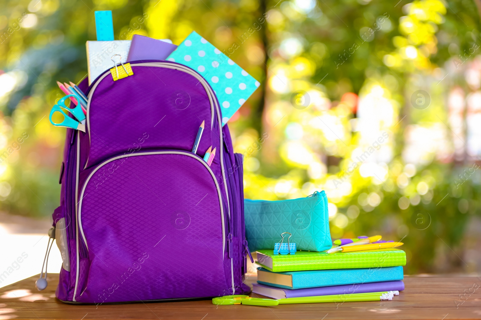 Photo of Backpack with school stationery on table outdoors