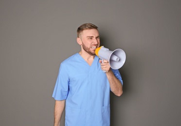 Photo of Male doctor shouting into megaphone on grey background