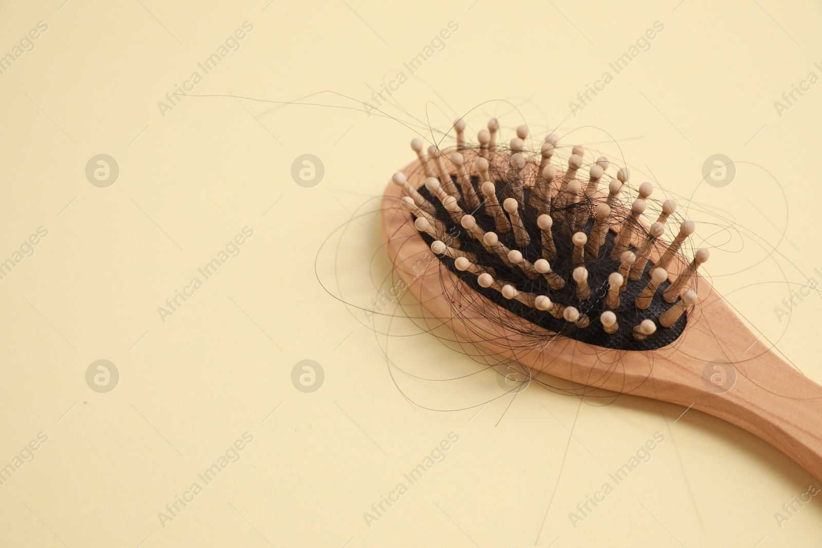 Photo of Wooden brush with lost hair on beige background, closeup. Space for text