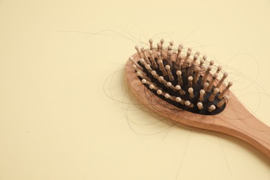 Photo of Wooden brush with lost hair on beige background, closeup. Space for text
