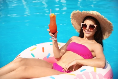 Photo of Beautiful young woman with cocktail and inflatable ring in swimming pool