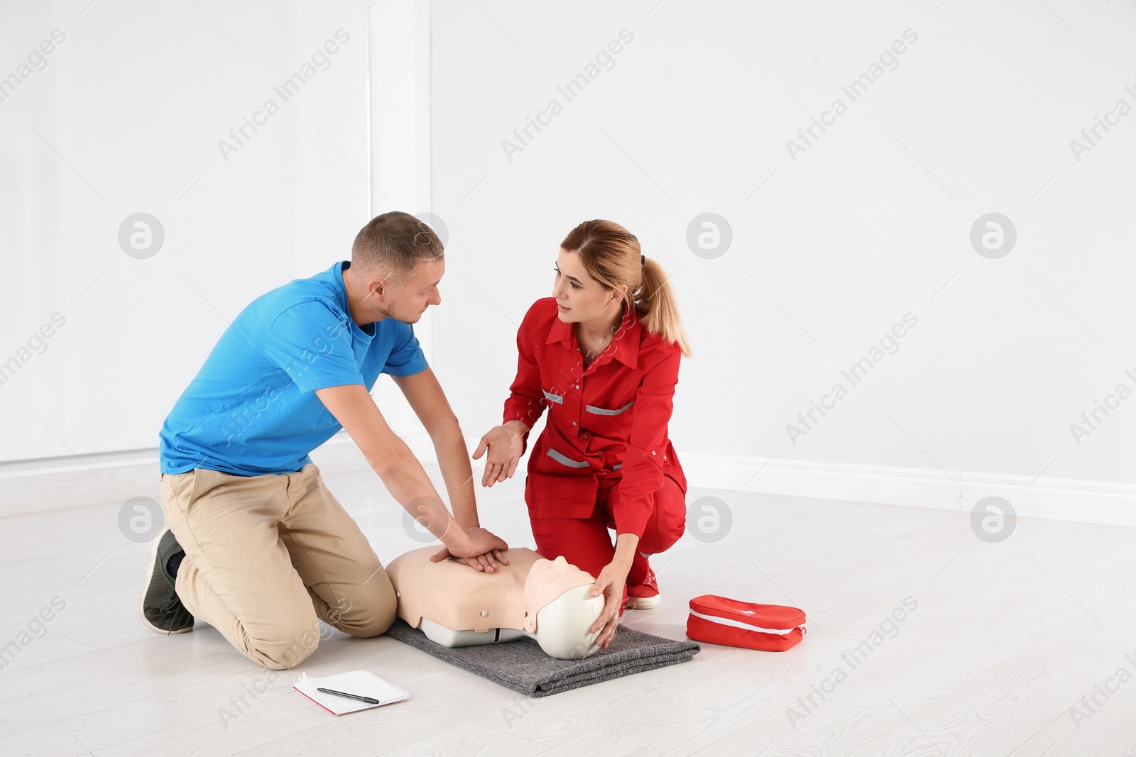 Photo of Instructor in uniform and man practicing first aid on mannequin indoors