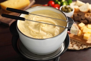 Photo of Fondue with tasty melted cheese, forks and piece of bread on table