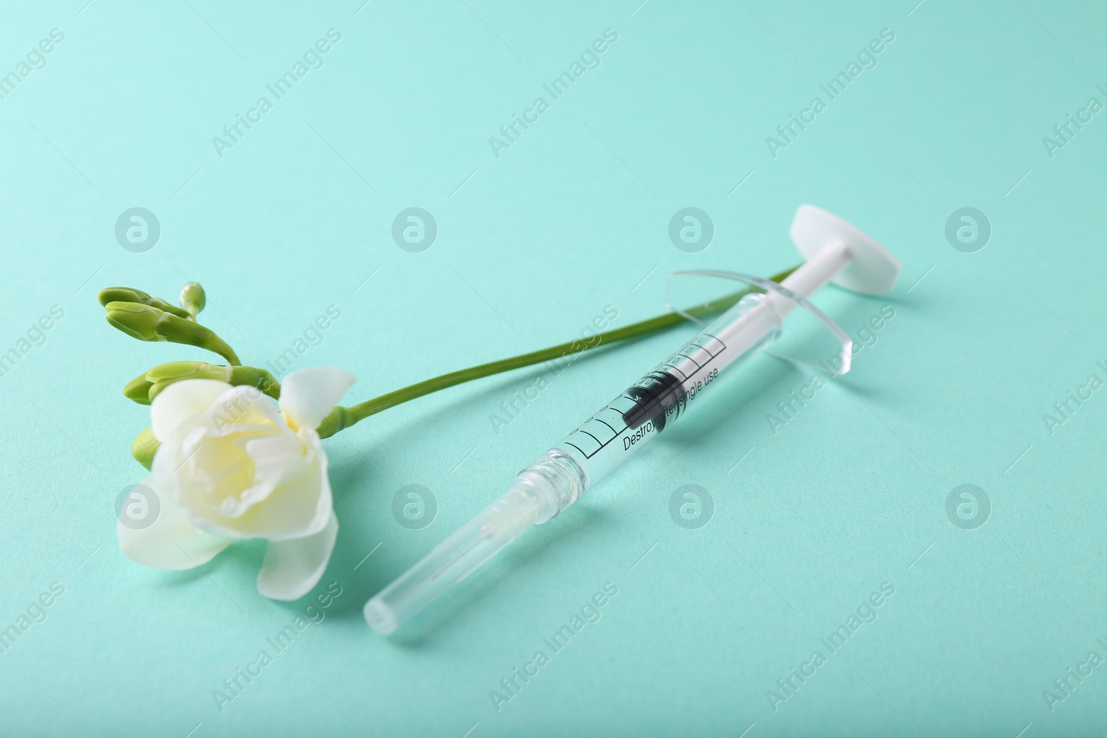 Photo of Cosmetology. Medical syringe and freesia flower on turquoise background