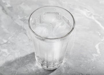 Glass of soda water with ice on grey table