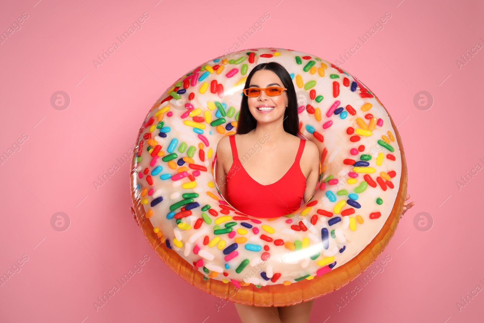 Photo of Young woman with stylish sunglasses holding inflatable ring against pink background