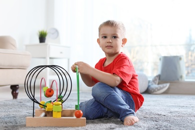 Cute child playing with bead maze on floor indoors