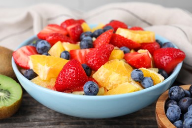 Photo of Delicious fresh fruit salad in bowl on wooden table, closeup