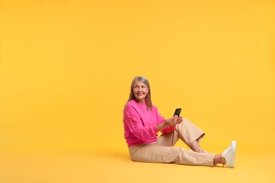 Senior woman with phone on orange background, space for text