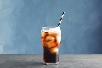 Glass of refreshing cola with ice on table against color background