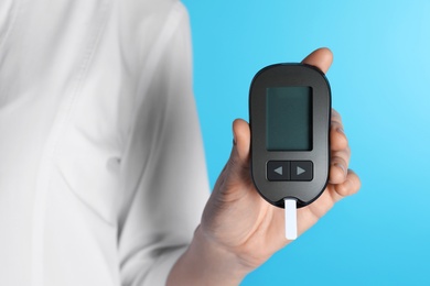 Photo of Female doctor holding digital glucometer on color background, closeup. Medical object