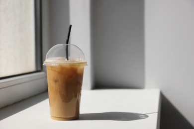 Photo of Plastic takeaway cupdelicious iced coffee on window sill indoors, space for text