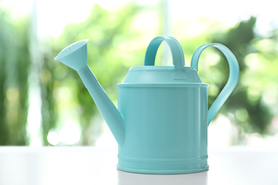 Photo of Light blue watering can on white table against blurred background