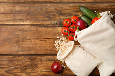 Photo of Cotton eco bags with vegetables and oat flakes on wooden table, flat lay. Space for text