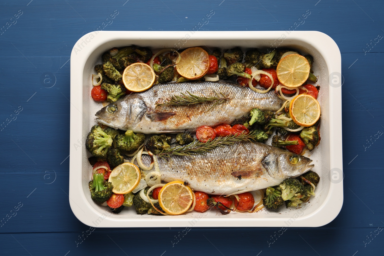 Photo of Delicious fish with vegetables and lemon in baking dish on blue wooden table, top view