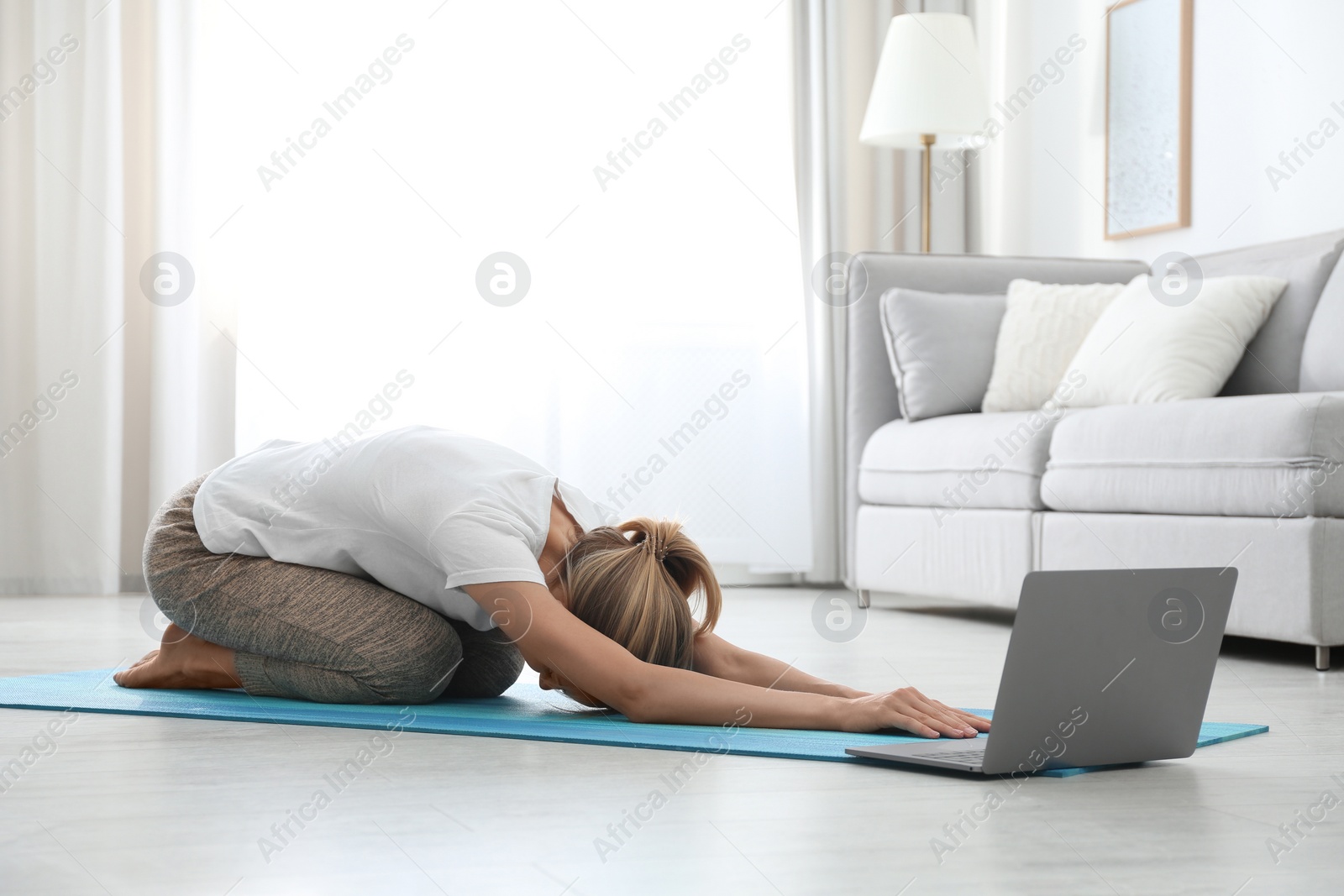 Photo of Woman having online video class via laptop at home. Distance yoga course during coronavirus pandemic