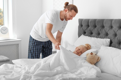 Photo of Caring father covering his sleeping daughter with blanket at home