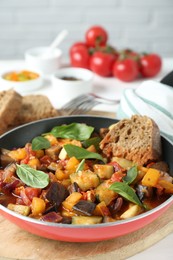 Photo of Dish with tasty ratatouille, bread and basil on wooden board, closeup