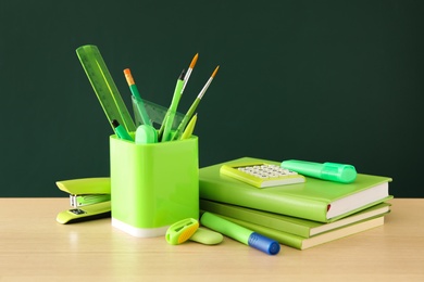 Photo of Different school stationery on wooden table near green chalkboard. Back to school