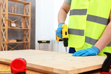 Photo of Young worker using electric drill at table in workshop, closeup