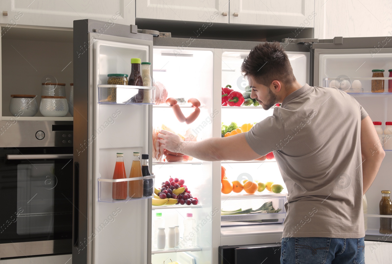 Photo of Young man taking ham out of refrigerator indoors, closeup