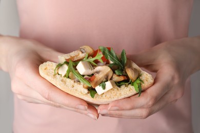 Photo of Woman holding delicious pita sandwich with cheese, mushrooms, tomatoes and arugula, closeup