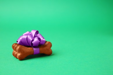 Photo of Bone shaped dog cookies with purple bow on green background, space for text