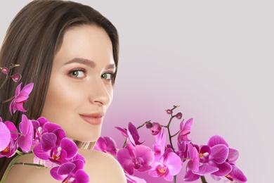 Image of Beautiful young woman and orchid flowers on light background, closeup view with space for text. Spa portrait