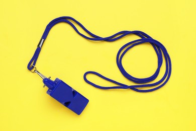 Photo of One blue whistle with cord on yellow background, top view
