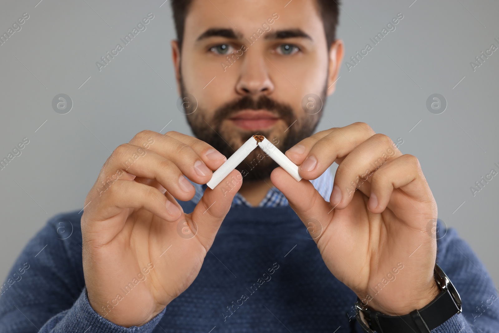 Photo of Stop smoking concept. Man breaking cigarette on light grey background, selective focus