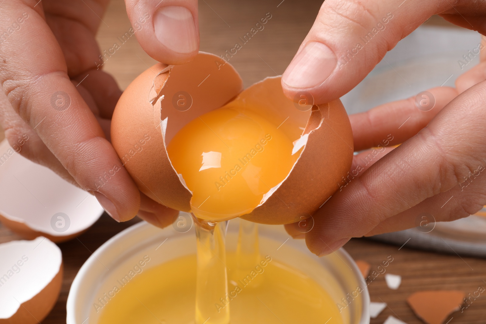 Photo of Woman separating egg yolk from white over bowl at table, closeup