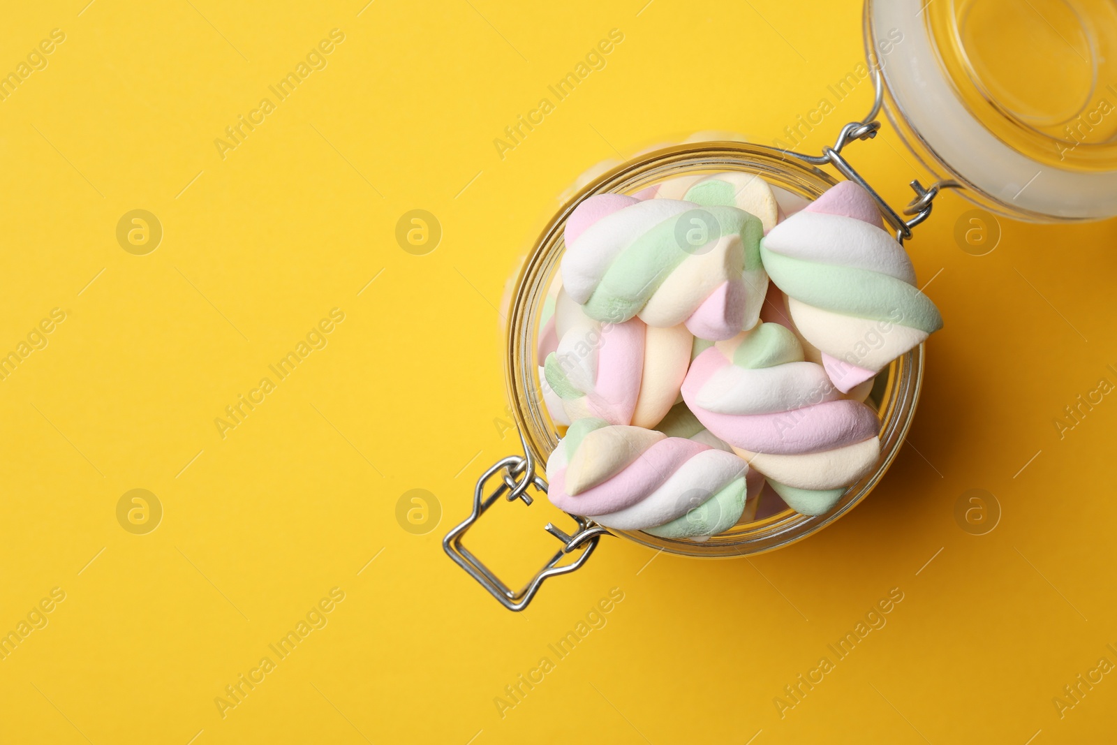 Photo of Jar of delicious colorful marshmallows on yellow background, top view. Space for text