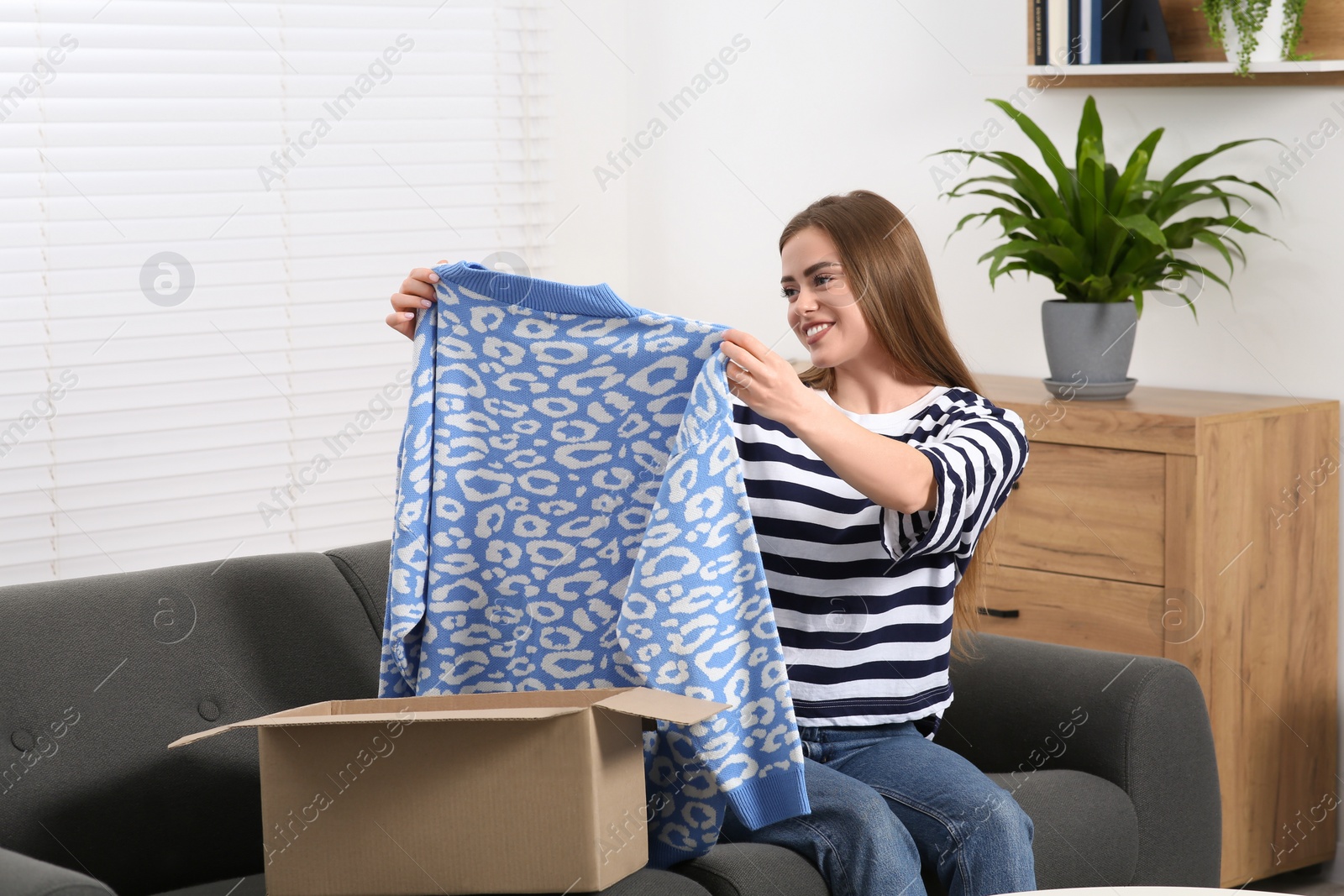 Photo of Happy woman with just unpacked new sweater at home. Online store