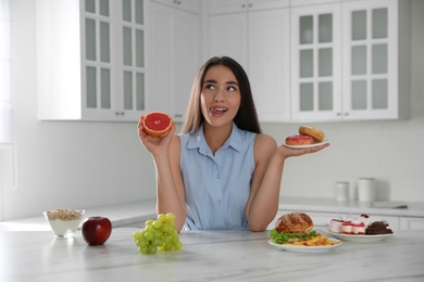 Photo of Woman choosing between grapefruit and doughnuts in kitchen