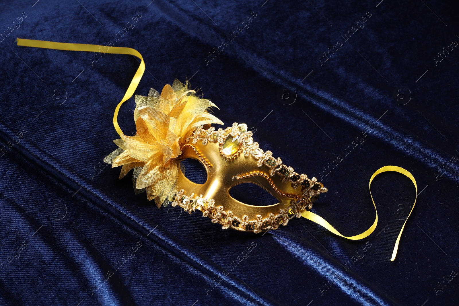 Photo of Theater arts. Golden venetian carnival mask on blue fabric, top view