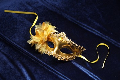 Photo of Theater arts. Golden venetian carnival mask on blue fabric, top view