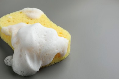 Yellow sponge with foam on grey background, closeup
