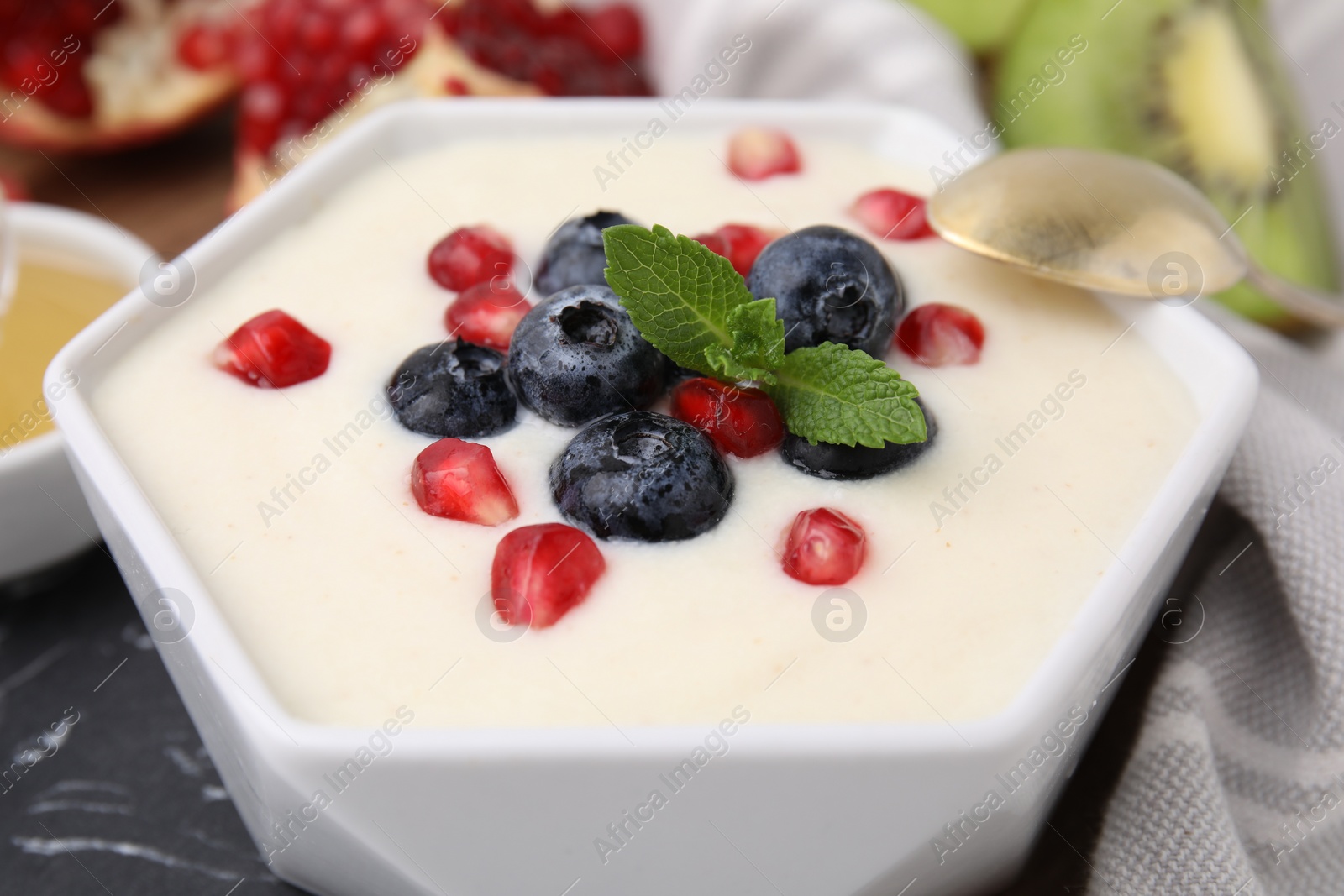 Photo of Bowl of delicious semolina pudding with blueberries, pomegranate and mint served on table, closeup